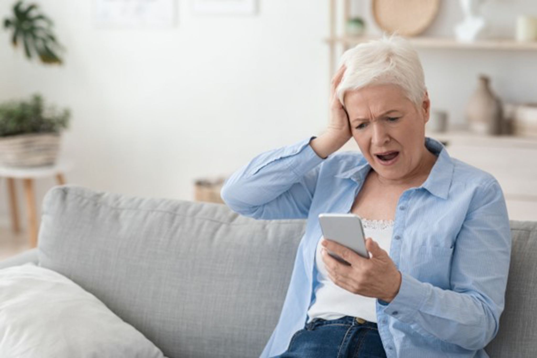 Elderly woman holding head and looking at phone