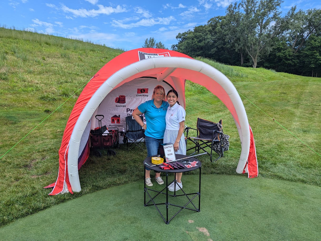 Volunteers stand in front of hole sponsor tent at golf course