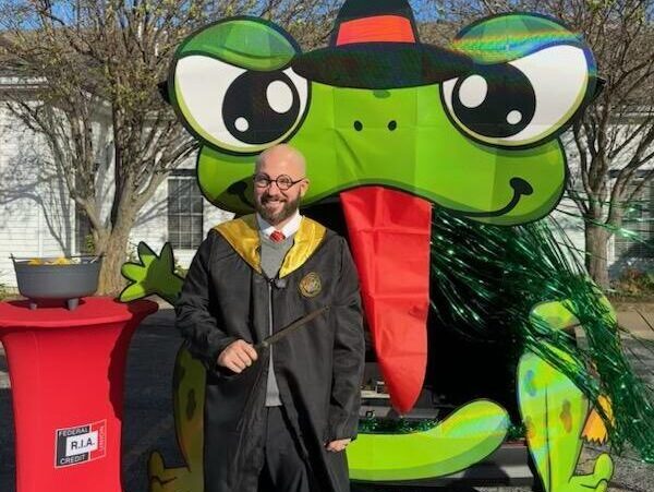 Man dressed as wizard in front of Halloween frog trunk or treat display